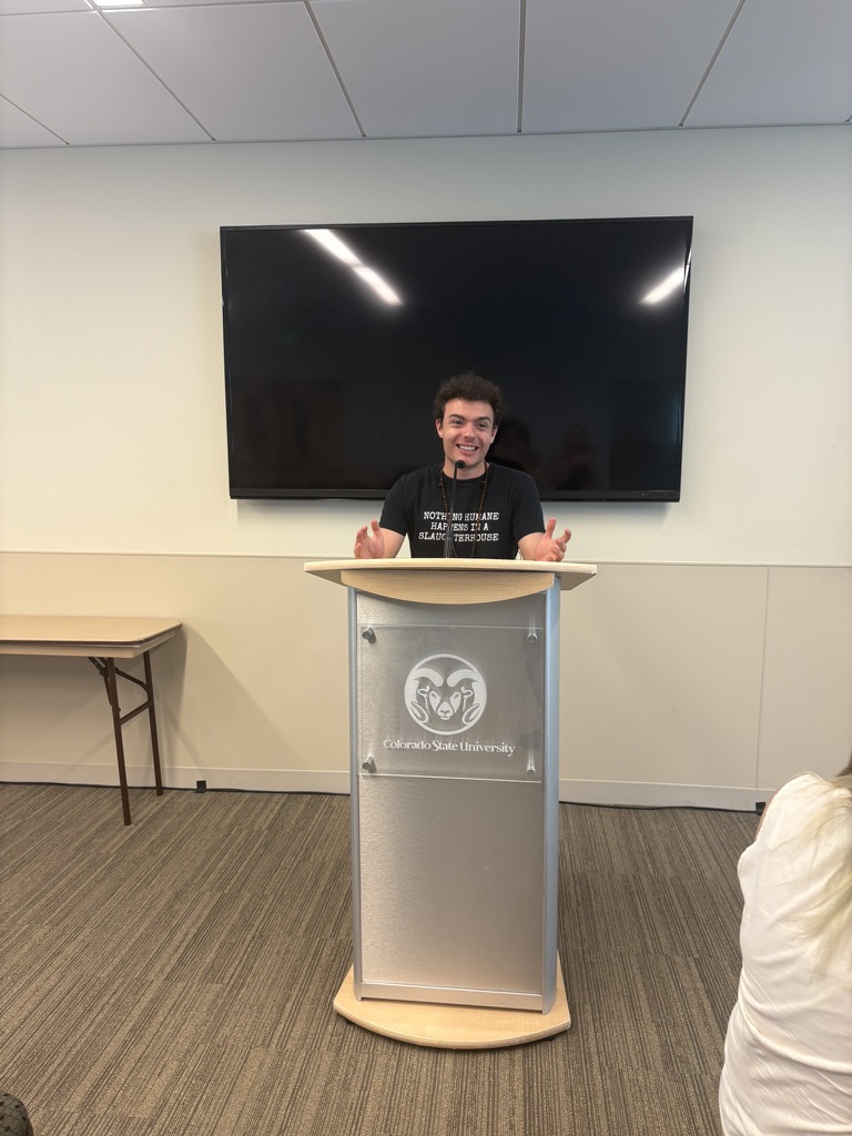 Samo standing at a podium in a classroom.